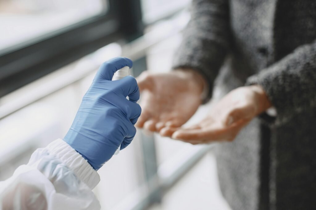 Close-up of a gloved hand using a spray bottle to disinfect a person's hands. Indoors setting.